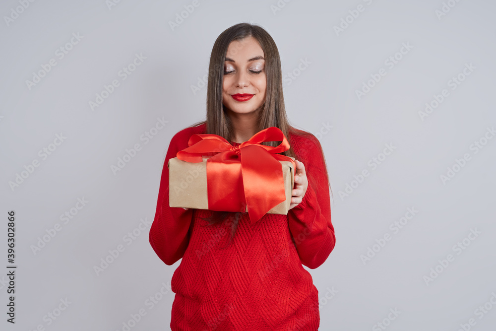 Lovely woman in a red sweater, holding a gift box, against a gray background, closing her eyes. Holiday concept, Christmas, New Year Lovely woman in a red sweater, holding a gift box, against a gray background, closing her eyes. Holiday concept, Christmas, New Year