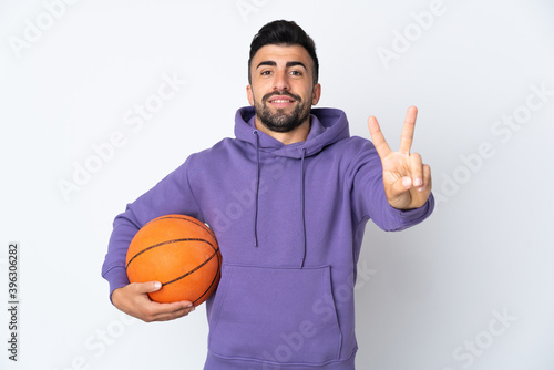 Man playing basketball over isolated white wall smiling and showing victory sign © luismolinero