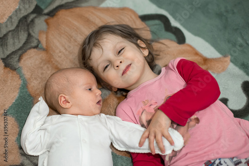 Two sisters - a three-year-old girl and a two-month-old baby-are lying on a blanket in the room.