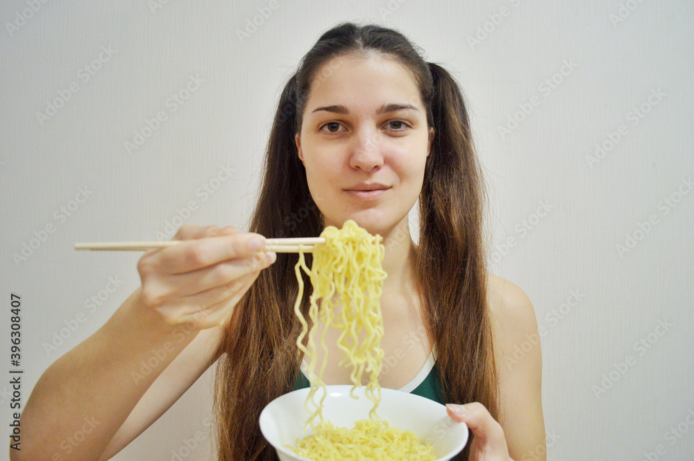Young girl eats instant noodles with wooden chopsticks on a light background Young girl eats instant noodles with wooden chopsticks on a light background