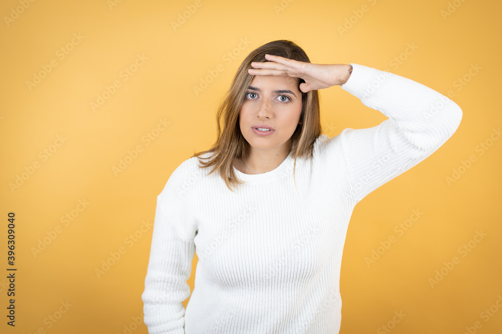 Young caucasian woman over isolated yellow background very happy and smiling looking far away with hand over head. searching concept. Young caucasian woman over isolated yellow background very happy and smiling looking far away with hand over head. searching concept.