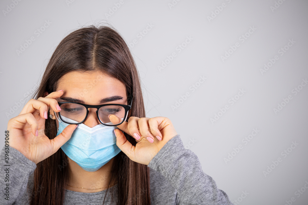 Woman wiping foggy glasses caused by wearing medical mask on gray background. Woman with foggy glasses caused by wearing disposable mask on gray background, space for text Woman wiping foggy glasses caused by wearing medical mask on gray background. Woman with foggy glasses caused by wearing disposable mask on gray background, space for text