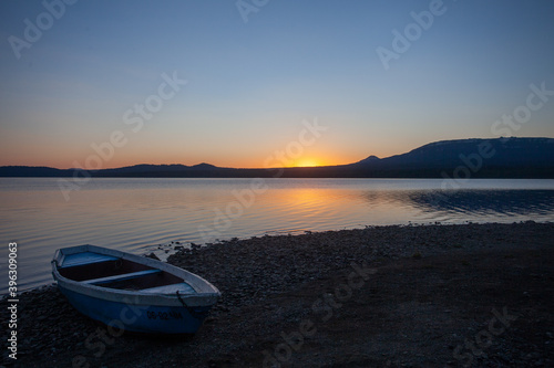 Wooden boat on the pebble shore of a mountain lake against the backdrop of a beautiful sunset