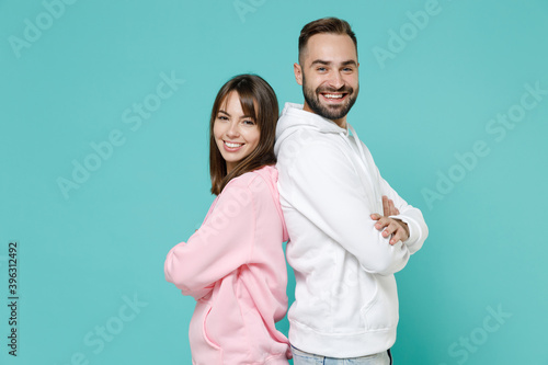 Side view of smiling young couple two friends man woman 20s in white pink casual hoodie standing holding hands crossed looking camera isolated on blue turquoise colour wall background studio portrait.