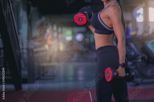 Young woman with sweat doing exercises  working out with dumbbell in fitness gym. Strong and healthy concept. Selected focus.