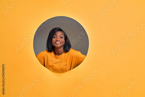 Portrait of a very happy and excited young  woman smiling in a round hole circle in orange background. Copy space. © HBS