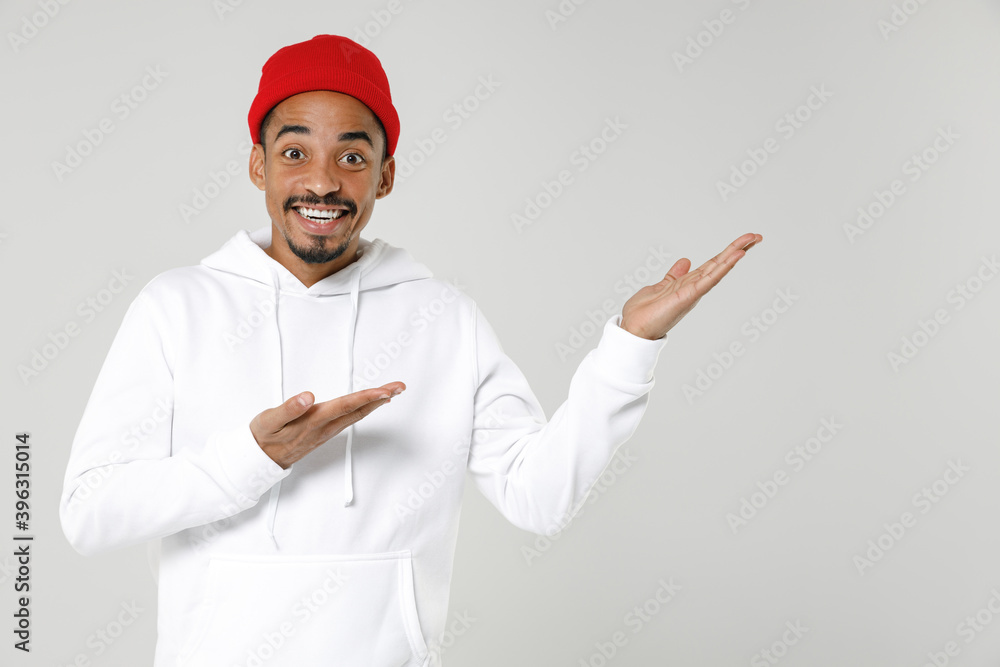 Excited cheerful smiling young african american man 20s wearing basic casual streetwear hoodie pointing hands aside on mock up copy space isolated on white colour wall background, studio portrait. Excited cheerful smiling young african american man 20s wearing basic casual streetwear hoodie pointing hands aside on mock up copy space isolated on white colour wall background, studio portrait.