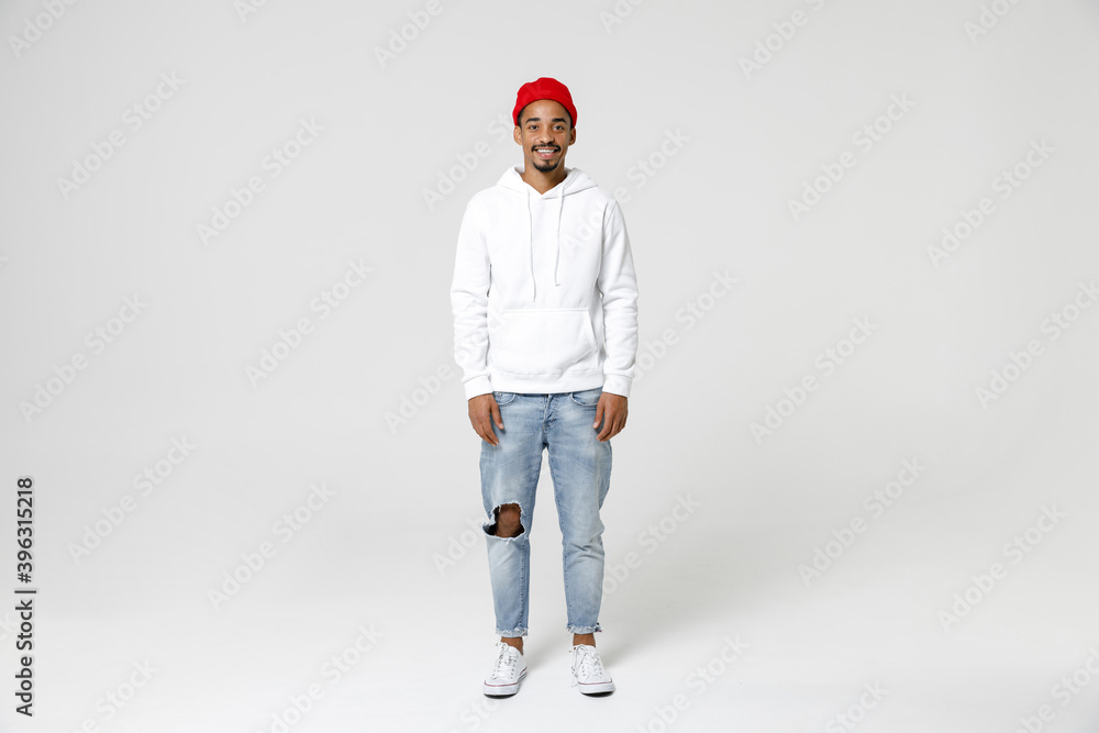 Full length of smiling cheerful handsome young african american man 20s years old in casual streetwear hoodie standing and looking camera isolated on white colour wall background, studio portrait. Full length of smiling cheerful handsome young african american man 20s years old in casual streetwear hoodie standing and looking camera isolated on white colour wall background, studio portrait.