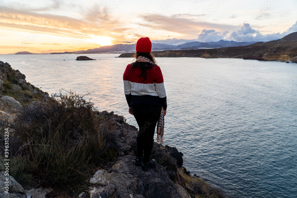 Obraz premium mujer chica al atardecer asomada a precipicio en el mar con gorro rojo y jersey de lana