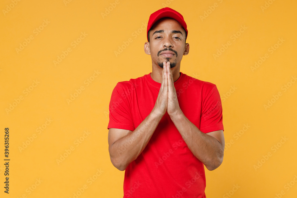 Delivery employee african man in red cap blank print t-shirt uniform workwear work courier service on quarantine covid-19 virus concept isolated on yellow background studio. Tattoo translation life.