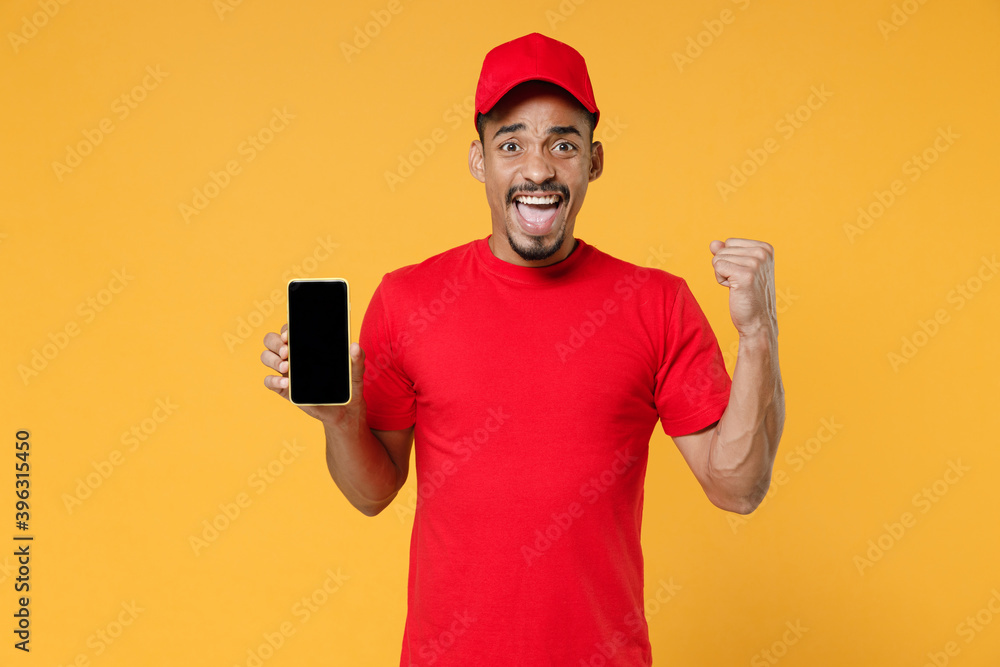 Delivery employee african man in red cap blank print t-shirt uniform workwear work courier service concept hold in hand using mobile cell phone free space screen isolated on yellow background studio. Delivery employee african man in red cap blank print t-shirt uniform workwear work courier service concept hold in hand using mobile cell phone free space screen isolated on yellow background studio.