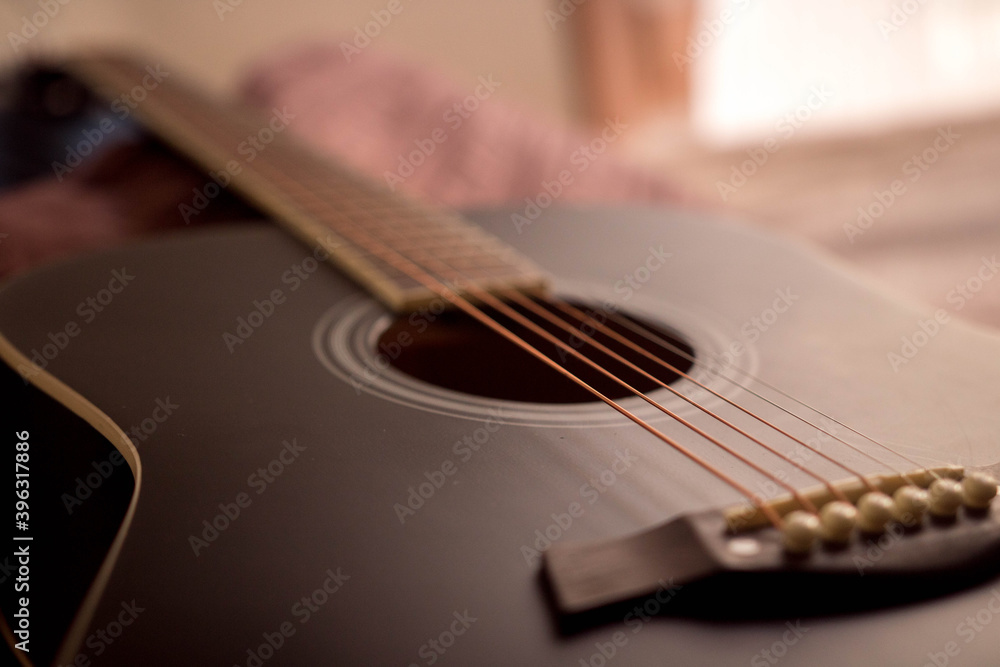 Fototapeta premium Black acoustic guitar on a bed a sunny day in a beautiful room