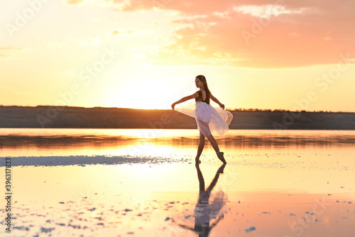 Tender girl young ballerina in a pink transparent skirt on the lake at sunset.