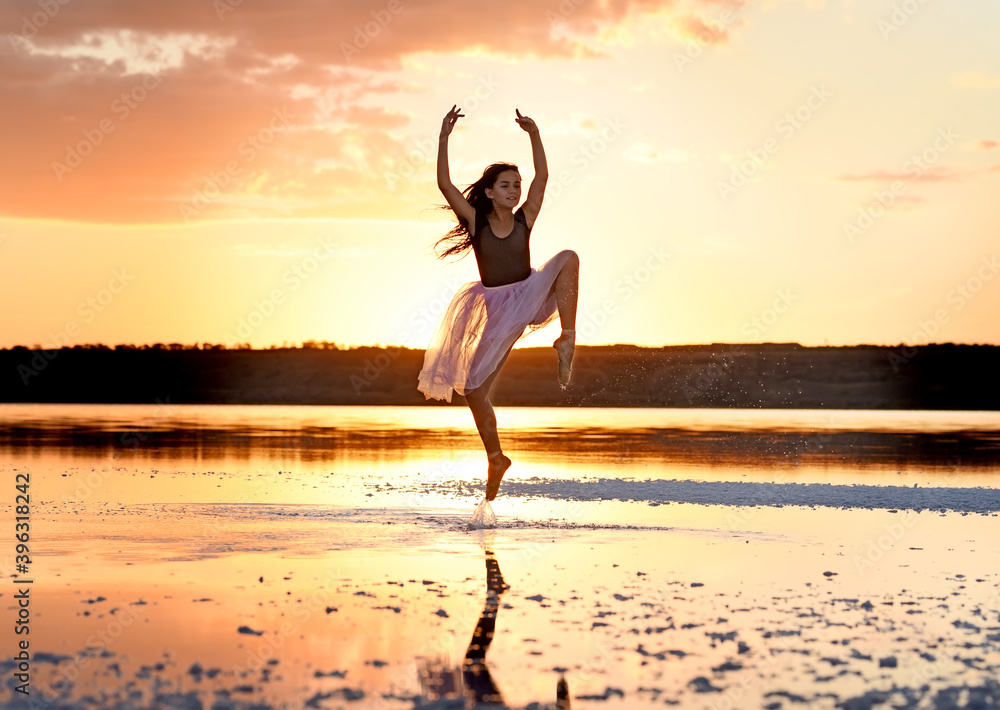 Tender girl young ballerina in pink transparent in a graceful jump on the lake at sunset.