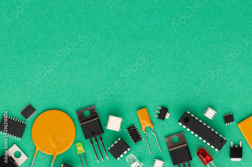 Electronic components over green background with copy space. There are microcontrollers, transistors, yellow and red LEDs, microcircuits, thyristors, capacitor.