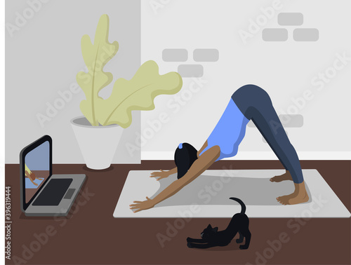 Happy sporty girl doing online yoga exercises on the mat at home during the quarantine period during the coronavirus pandemic. The cat does yoga with the girl .. An active healthy woman enjoys sports,