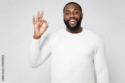 Excited cheerful funny handsome attractive young african american man 20s wearing casual basic sweater standing showing Ok gesture looking camera isolated on white color background studio portrait.