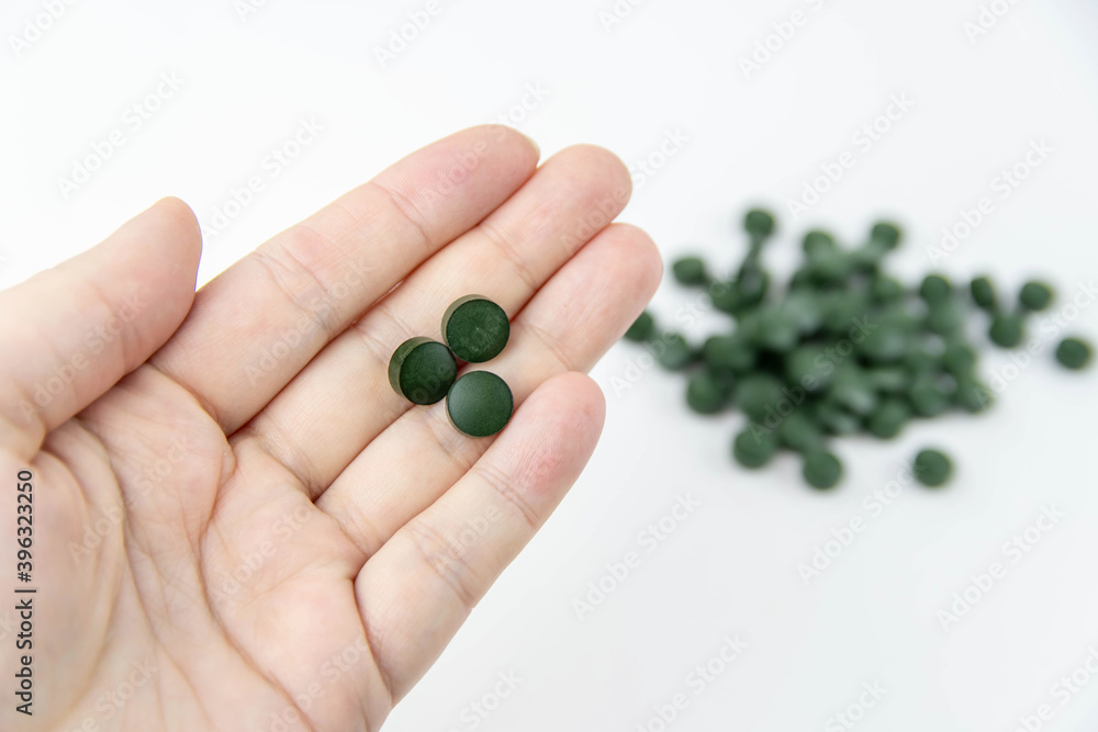 Φωτογραφία A female hand holds three green pills, vitamins spirulina, a bunch of green pills out of focus