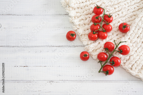 two branches of red tomatoes cherry on white knited surface, wooden background. Copy space. Selective focus.