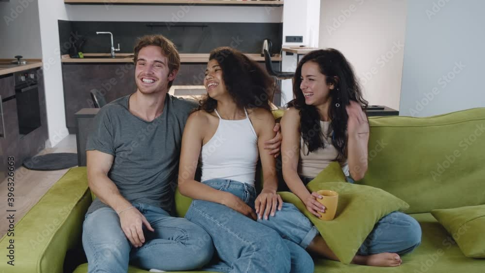 Happy group of young man and two women talking, and watching TV. Friends choose genre of the movie comedy or horror, together while sitting on the couch. Mixed race young people have a party at home Happy group of young man and two women talking, and watching TV. Friends choose genre of the movie comedy or horror, together while sitting on the couch. Mixed race young people have a party at home