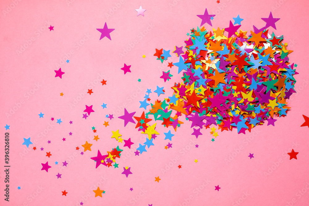 Flat lay frame background of multicolored sparkle confetti glittering shine stars isolated on pink. Top view. For Christmas, holiday, festive, sales.