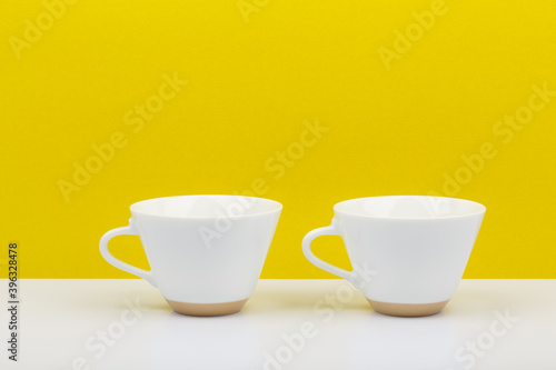 Two white cups of coffee in a row against yellow background. Still life with a space for text
