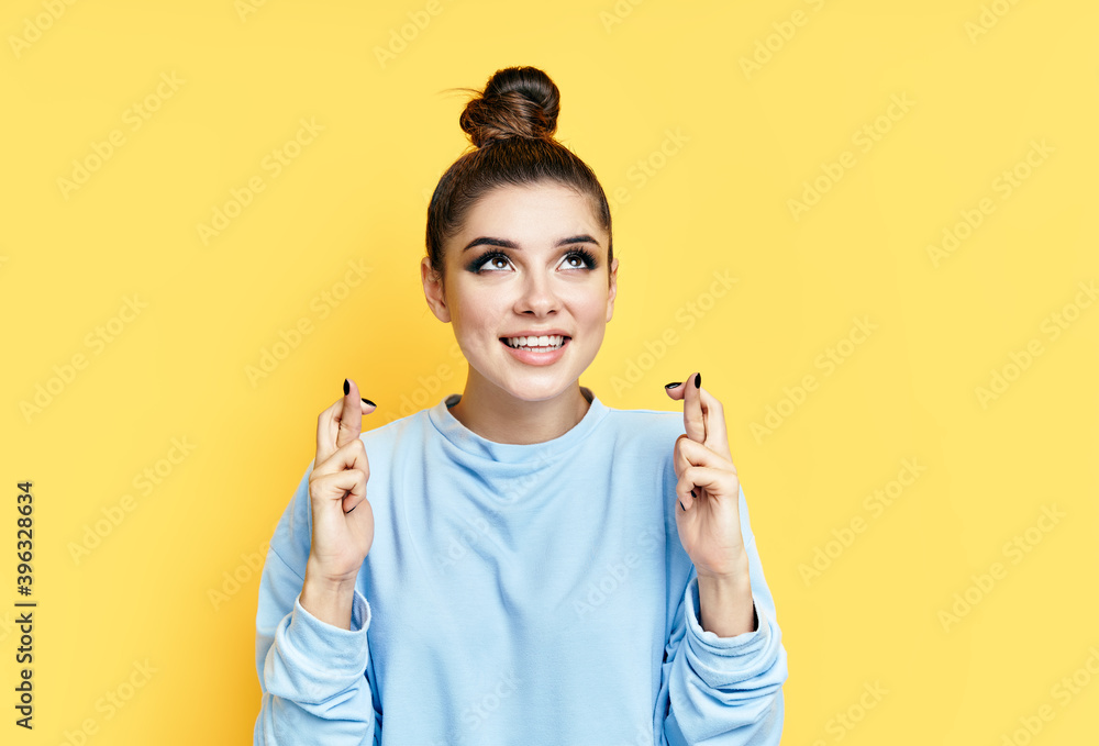 Young beautiful woman crossing her fingers and wishing for good luck over yellow background. Young beautiful woman crossing her fingers and wishing for good luck over yellow background.