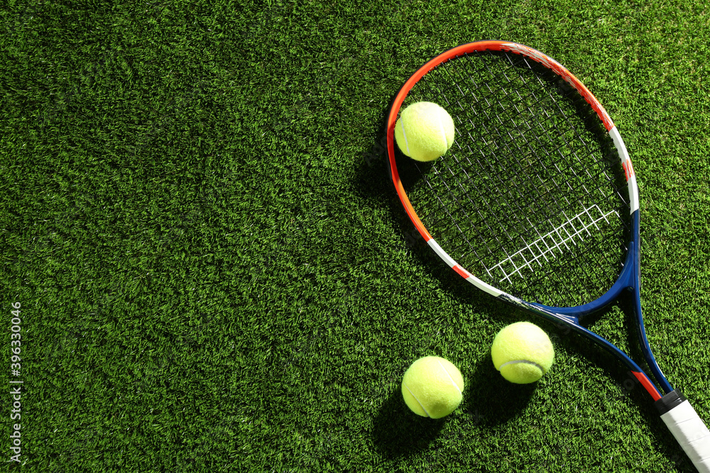 Tennis racket and balls on green grass, flat lay. Space for text