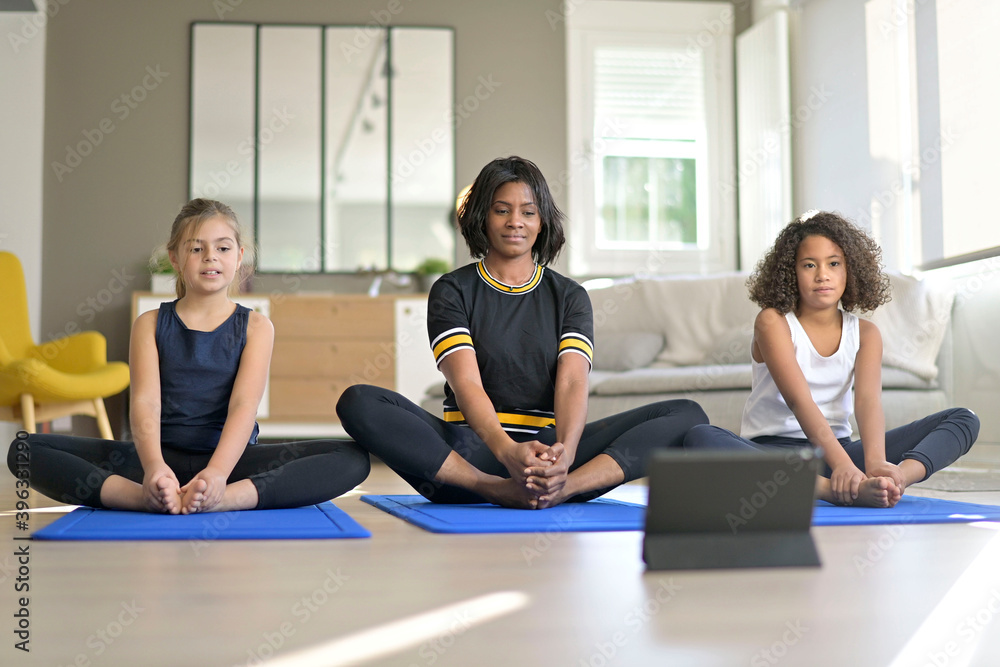 Obraz premium Young woman with kids doing fitness exercices at home, online class