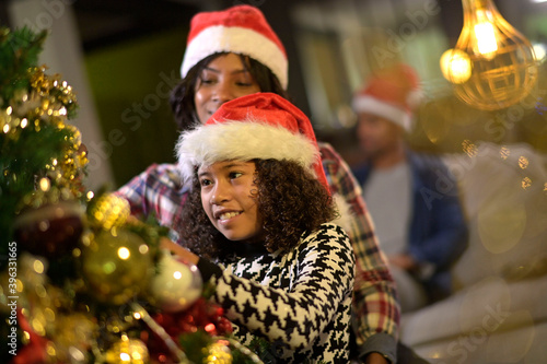 Mother and daughter with santa hat decorating christmas tree together