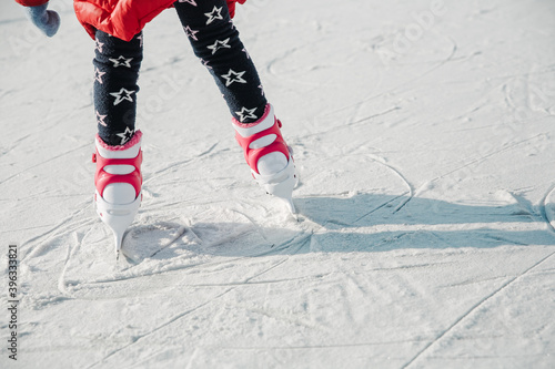 Figure skates on girl legs on ice covered with snow and with traces made by skating. Child winter outdoors on ice rink. Ice and legs