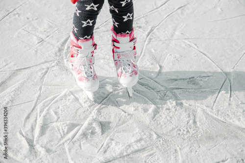 Figure skates on girl legs on ice covered with snow and with traces made by skating. Child winter outdoors on ice rink. Ice and legs photo