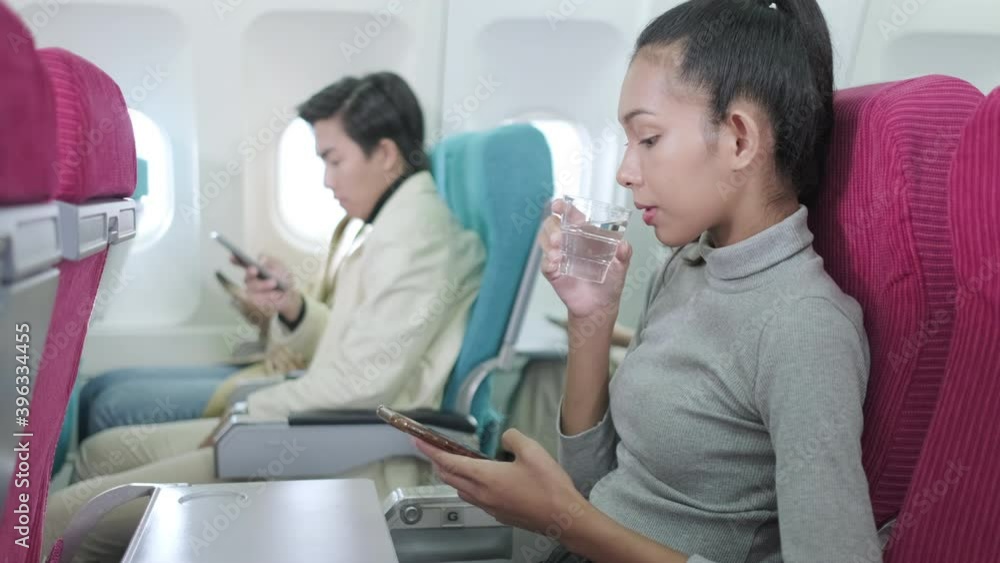Asia passenger woman drinking a cup of water during flight and look at smartphone for social network before take off. Flying in economy seat airplane flight. Feeling excite for first time flight Asia passenger woman drinking a cup of water during flight and look at smartphone for social network before take off. Flying in economy seat airplane flight. Feeling excite for first time flight