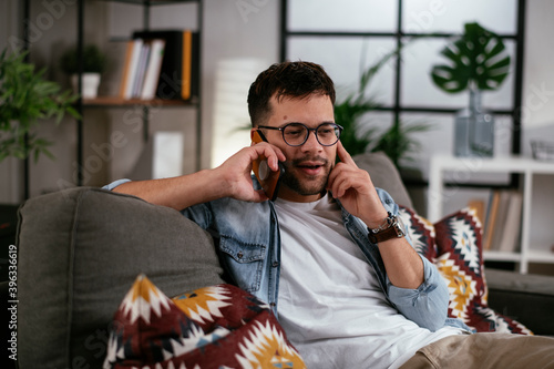 Young man talking on the phone while sitting on sofa. Happy man using the phone. photo