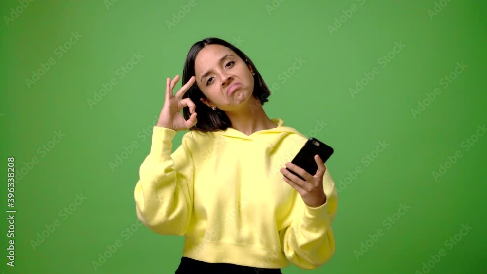 Young woman using mobile phone on green screen chroma key background showing ok sign with fingers Young woman using mobile phone on green screen chroma key background showing ok sign with fingers