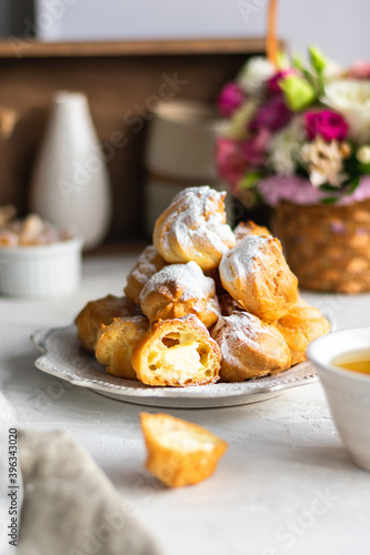Homemade profiteroles with cream in a gray plate on a white table. Basket with fresh flowers photo
