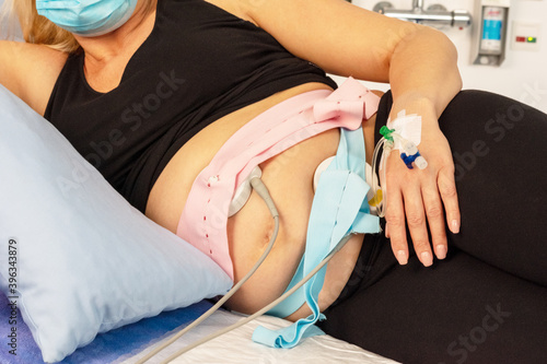 Schwangere während der Corona-Pandemie in einem Zimmer im Krankenhaus mit angelegten CTG und Venenkatheter