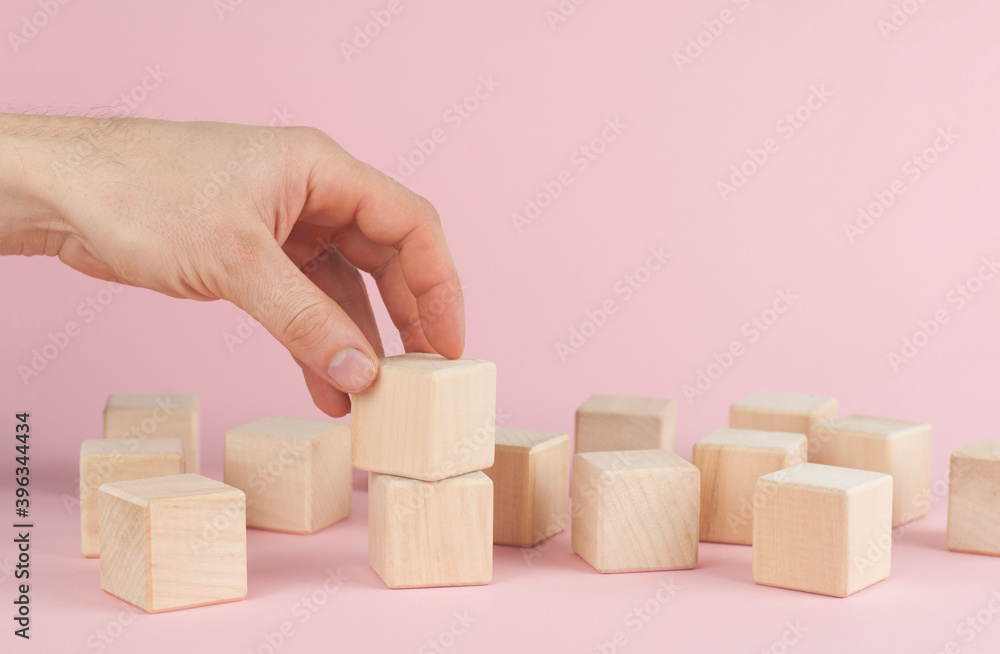 Obraz premium Wooden cubes on a pink background. The hand puts the cube. Place for text