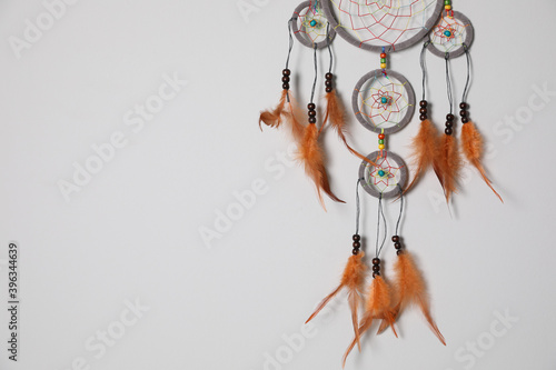 Beautiful dream catcher hanging on white wall. Space for text