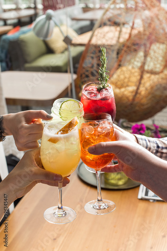 Friends toasting saying cheers hands holding summer cold cocktail drinks on cafe background