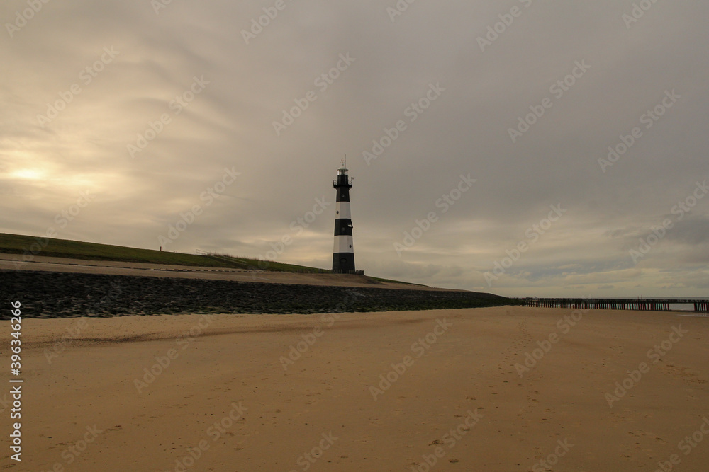 a coast landscape with a large sand beach and a lighthouse at the seawall and a grey sky in winter in breskens