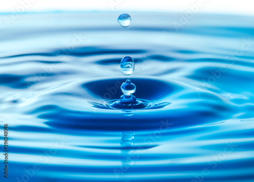 Dark blue water droplets splash in the water surface close up. Creating a perfect water wave