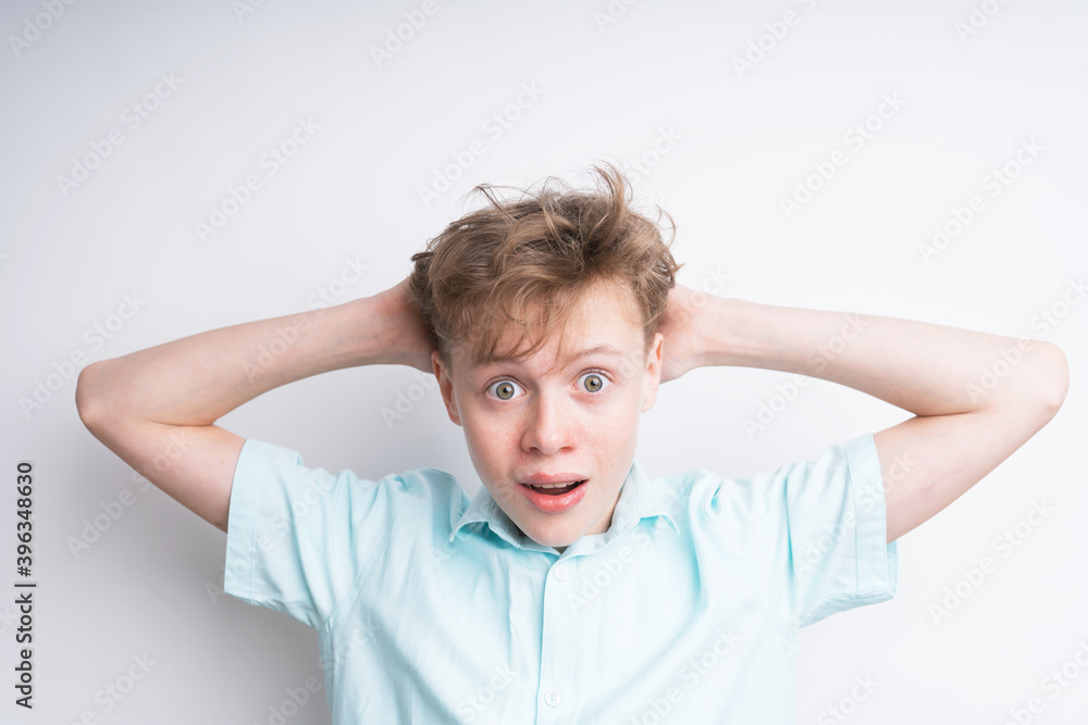 A mid shot of a surprised Caucasian boy in a blue shirt holding hands behind his head. His mouth is wide open and so his eyes A mid shot of a surprised Caucasian boy in a blue shirt holding hands behind his head. His mouth is wide open and so his eyes
