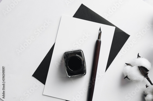 Set of vintage dip pen, inkpot and blank paper sheet with envelope on white wooden table