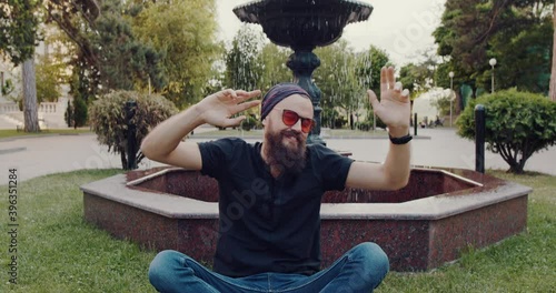 a young hipster man with a beard and glasses, sitting on the grass in the park