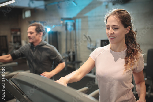 Determined and focused young mixed ethnicity couple jogging on treadmills in modern indoor gym