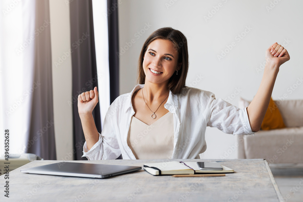 Obraz premium Beautiful brunette woman has completed business project, is happy. Girl sits at desk in home office. Distance work