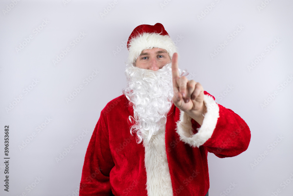 Man dressed as Santa Claus standing over isolated white background showing and pointing up with fingers number one while is serious Man dressed as Santa Claus standing over isolated white background showing and pointing up with fingers number one while is serious