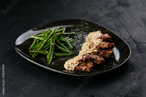 marbled beef steak with vegetables and sauce on a black backgrou photo