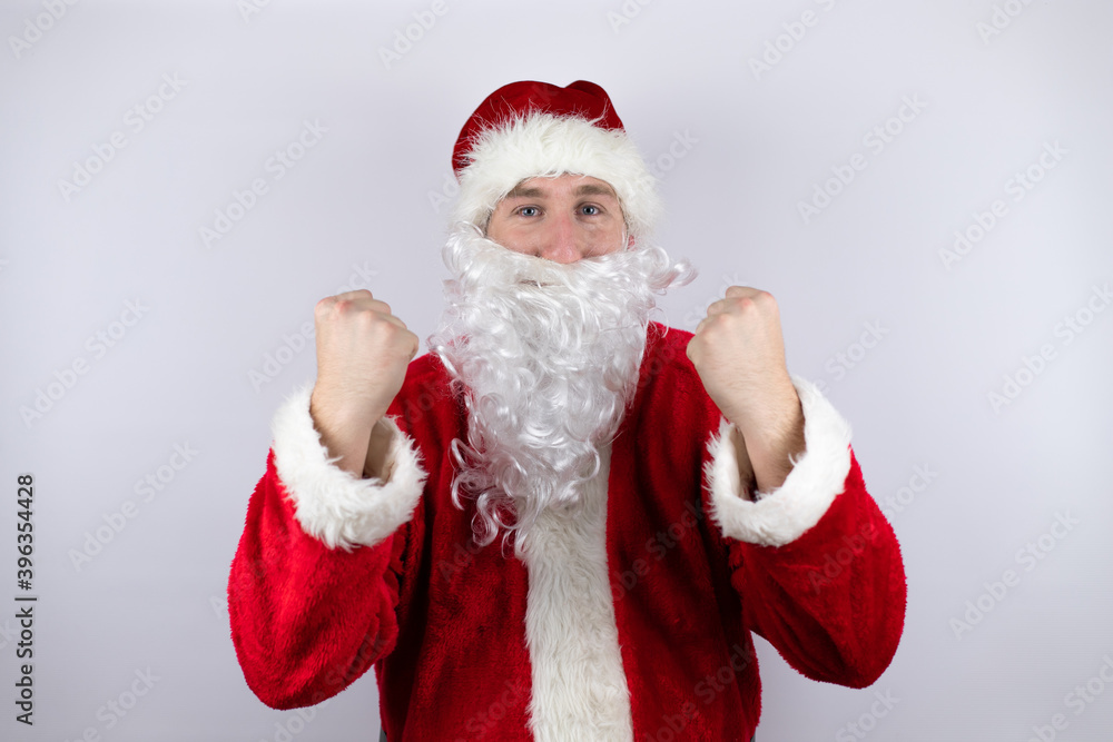 Man dressed as Santa Claus standing over isolated white background very happy and excited making winner gesture with raised arms, smiling and screaming for success.